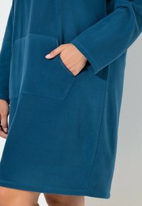 Fleece kjole i mørkeblå, med en frontlomme, lange ærmer og en afslappet silhuet. Blød tekstur og kant lige over knæet.