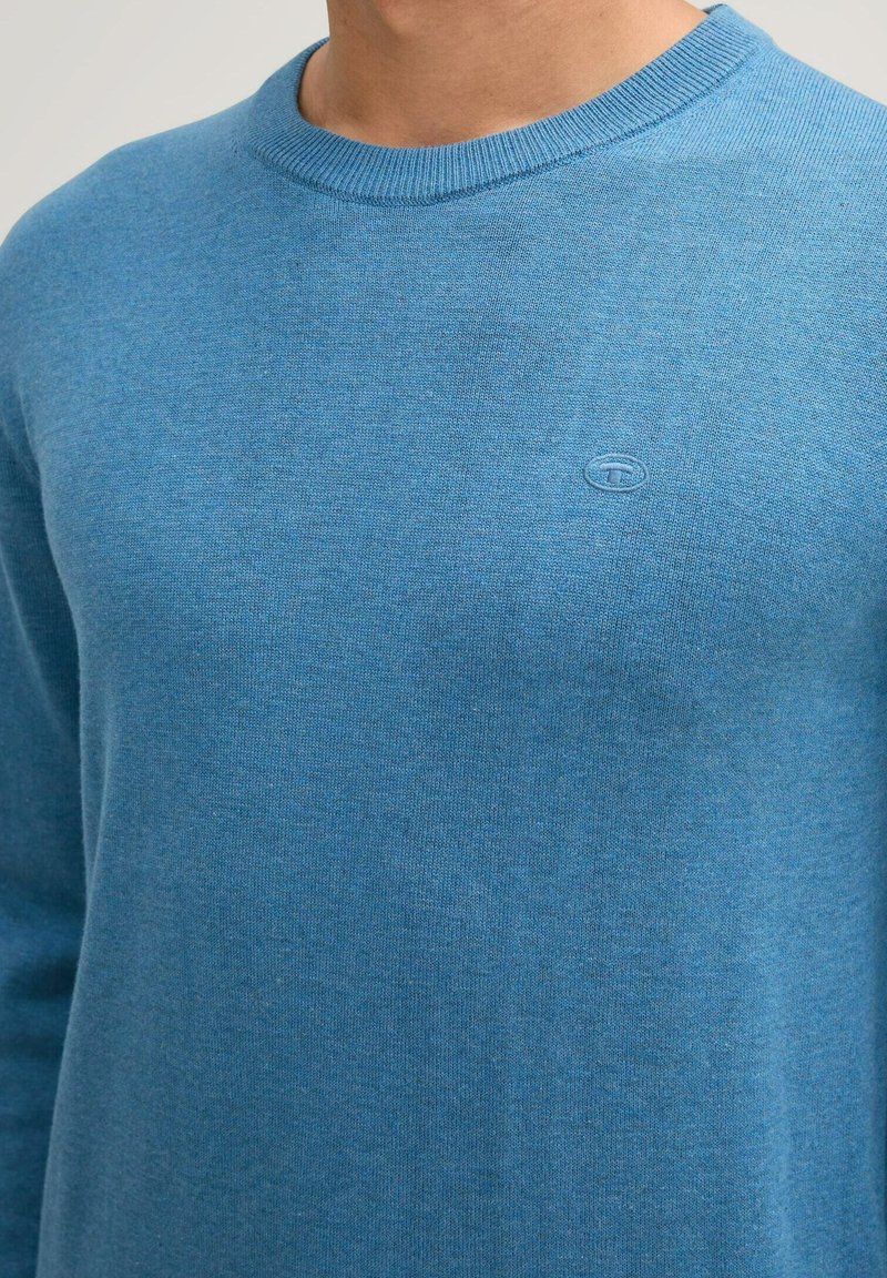 Pullover blu a maglia con scollatura rotonda e polsini a costine. Presenta un piccolo logo sul petto. Tessuto morbido e vestibilità casual.