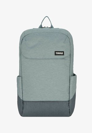 Sac à dos en tissu bleu clair avec une poignée supérieure, une poche avant, des poches latérales et un fond gris foncé. Il présente un logo noir bien visible.