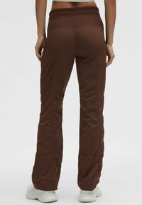 Bruine sportieve broek met een geribbelde textuur, brede elastische tailleband, rechte pijpen en subtiele zijzakken, gecombineerd met witte sneakers.