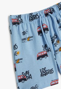 Lyseblå shorts lavet af blødt stof, med et mønster af røde vans, palmetræer, surfbrætter, sol og tekst der læser "Los Angeles" og "Surf Day."