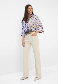 Blauwe en paarse blouse met een patroon en losse mouwen, geknoopt in de taille, gecombineerd met crèmekleurige flared broek en lichte schoenen.