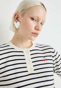 Stripete genser laget av mykt stoff med marineblå og hvite horisontale striper, med en knappeåpning i halsen og røde kirsebærbroderidetaljer.