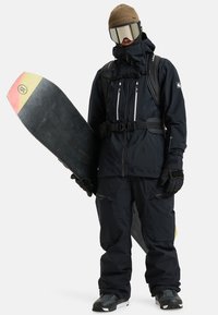 Schwarze Snowboarder-Außenbekleidung besteht aus einer wasserdichten Jacke mit mehreren Reißverschlusstaschen, kombiniert mit passenden Hosen und schwarzen Handschuhen. Snowboard ist im Lieferumfang enthalten.