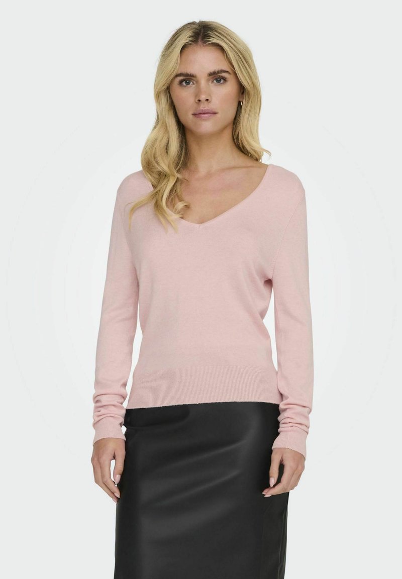 Helles rosa V-Ausschnitt-Pullover mit langen Ärmeln, aus weichem, strukturiertem Stoff; kombiniert mit einem eleganten schwarzen Rock.