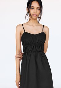 Robe noire sans manches avec une taille élastique, présentant un décolleté en cœur et un tissu doux. Le design est simple, sans motifs ni accents.