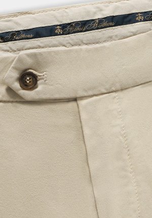 Beige katoenen broek met een klassiek ontwerp, knoopsluiting en een gladde textuur. De binnenband heeft een donkerblauw label met gouden tekst.