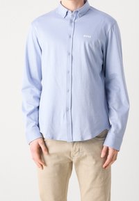 Ljusblå långärmad skjorta med krage, i ett strukturerat tyg och med en liten vit logotyp på vänster bröst.