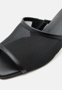 Μαύρο σανδάλι mule ανοιχτής μύτης με επάνω μέρος από δίχτυ και δερμάτινη επένδυση, με τετράγωνη μύτη και χαμηλό τακούνι.