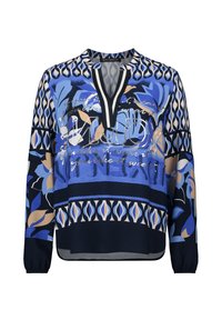 Blouse à motifs bleus à manches longues, avec des dessins floraux en bleu, crème et marine, un décolleté en V profond et une texture de tissu douce.