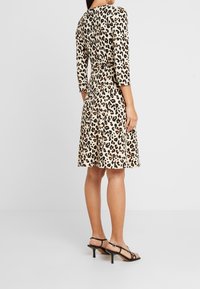 Sukienka w panterkowy wzór z kremowej tkaniny. Posiada rękawy o długości trzy czwarte, dopasowaną talię i rozkloszowany dół. Połączona z czarnymi sandałami na obcasie.