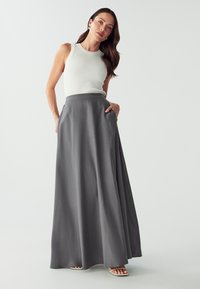 Maxi skirt in gray fabric with a smooth texture, high waist, and side pockets. Paired with a fitted white sleeveless top.