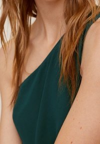 Robe verte à une épaule en tissu doux, présentant un design fluide et une texture lisse, mettant en valeur l'épaule.