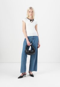 White short-sleeve top with a black collar accent, paired with blue wide-leg jeans and black pointed-toe heels, holding a black handbag.