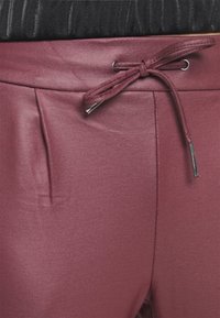 Burgundy, släta tygbyxor med dragsko i midjan, med sidofickor och metalldetaljer på snörningen. Mjuk textur med en åtsittande silhuett.