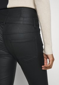 Svarta, åtsittande jeans med en slät yta, som har en bakficka och sömdetaljer. Bärs tillsammans med en ljus, ribbad tröja.