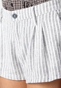Bílo-šedé pruhované šortky vyrobené z lehkého materiálu, obsahující plisování, zapínání na knoflík a boční kapsy.