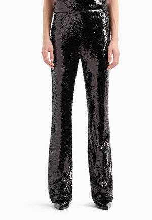 Pantaloni neri di paillettes con gambe svasate, con una superficie lucida e testurizzata che riflette la luce. Design slim fit, abbinati a scarpe nere.