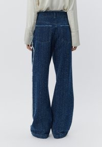 Spodnie dżinsowe o szerokich nogawkach w kolorze niebieskim z teksturowanym wykończeniem, z tylnymi kieszeniami i postrzępionymi bocznymi szwami, zestawione z lekkim topem z długim rękawem.