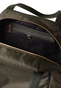 Intérieur de sac à dos vert texturé, avec une poche zippée et un revêtement en tissu noir, des fermetures éclair dorées et des accents en cuir.