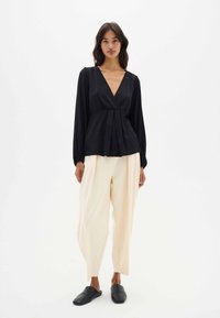 Blusa negra ajustada con mangas largas y escote en V profundo, combinada con pantalones anchos color crema y zapatos negros de tipo slip-on. Textura de tela suave.