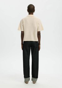 Krémový top z vlněné směsi s krátkými rukávy, doplněný tmavými džínami s ohrnutými lemy a minimálním zdobením.