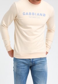 Sudadera beige con un escote redondo, mangas largas y un logo azul "GABBIANO THE URBAN LIFE". Tejido suave con puños acanalados.