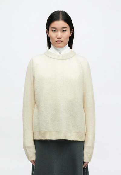 Κρεμ μάλλινο πουλόβερ φτιαγμένο από μαλακό υλικό, με στρογγυλή λαιμόκοψη, ρίγες στους ώμους και ριμπ μανσέτες και τελείωμα.