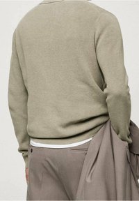 Gebreide trui in licht olijfgroen, met een gestructureerd oppervlak, ronde hals en een losse pasvorm. Gecombineerd met grijze geplooide broek.