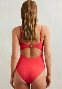 Rood een-piece badpak met verstelbare bandjes, open rugdesign en een gladde textuur. Heeft een midden-hoge beenuitsnijding en minimale hardware.
