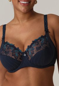 Granatowy biustonosz z koronkowymi detalami, przezroczysta siateczka u góry, haftowane kwiatowe akcenty w odcieniu teal oraz centralny ozdobny guzik.