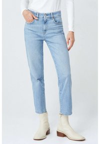 Jeans de tiro alto en azul claro con un diseño de pierna recta, que cuentan con bolsillos frontales y cremallera, combinados con botines crema.