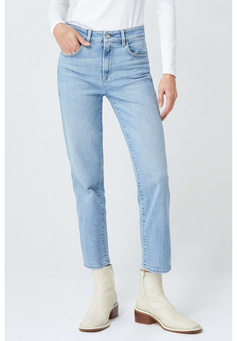 Jeans de tiro alto en azul claro con un diseño de pierna recta, que cuentan con bolsillos frontales y cremallera, combinados con botines crema.