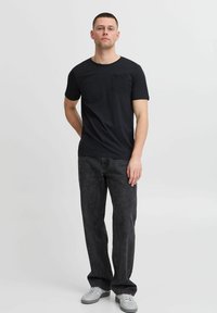 Camiseta negra de manga corta con bolsillo, combinada con pantalones gris oscuro y zapatillas blancas. Diseño simple, material de algodón, forma ajustada.