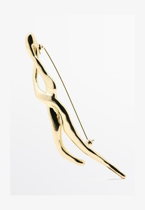 Broche dorée présentant un design abstrait de figure humaine avec une texture polie et lisse, et une épingle au dos pour le maintien.