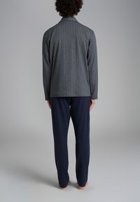 Giacca grigia a righe con una vestibilità su misura, abbinata a pantaloni blu navy. Entrambi hanno una consistenza liscia e una silhouette rilassata.