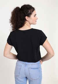Camiseta negra corta con mangas cortas enrolladas, hecha de una tela suave, combinada con jeans de tiro alto azul claro que tienen bolsillos traseros.
