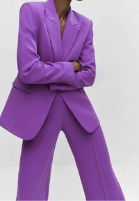 Traje morado hecho a medida que incluye una chaqueta estructurada con solapas de muesca y pantalones de pierna ancha, confeccionado con una tela suave y acabado mate.