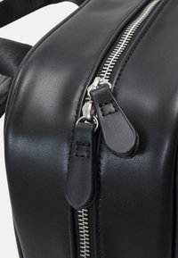Bolso de cuero negro con una textura suave, cremallera plateada con tiradores y costuras en contraste a lo largo de las costuras.