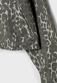 Jakna s uzorkom leopard u prigušenim zelenim i sivim tonovima, s vidljivim džepom i teksturiranim materijalom koji podsjeća na traper.