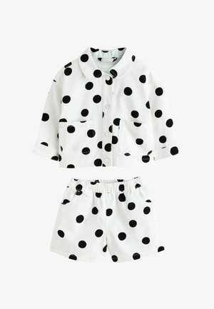 Valkoinen puuvillainen asu, jossa on kauluksellinen takki ja siihen sopivat shortsit, molemmissa mustat pilkut ja etutaskut, joustava vyötärönauha.