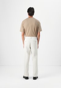 Beige bomulds t-shirt og lys grå bukser med lige snit og baglommer, parret med sorte sko. Neutrale nuancer og afslappet design.