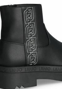 Stivale alla caviglia nero con tomaia in pelle strutturata, dettaglio del logo in rilievo argentato e suola in gomma spessa con bordo decorato.