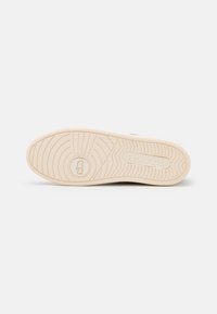 Semelle de chaussure avec semelle extérieure en caoutchouc beige, motifs de bande de roulement circulaires et linéaires, et logo « Coach » embossé près du talon et au centre.