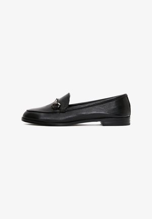 Mocassins en cuir noir avec un talon plat, dotés d'une languette rabattue et d'un accent métallique à l'avant. Texture lisse et design simple.