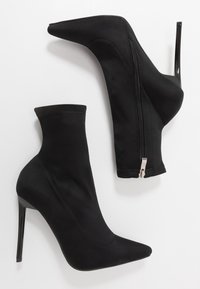 Stivali alla caviglia neri realizzati in morbido tessuto con punta appuntita, alto tacco a stiletto e dettaglio con zip laterale. Texture liscia e design minimalista.