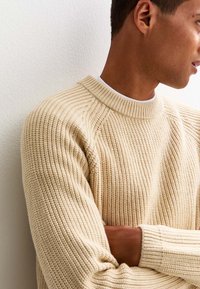 Beige gestrickter Pullover mit einem gerippten Muster, Rundhalsausschnitt und langen Ärmeln in entspannter Passform.