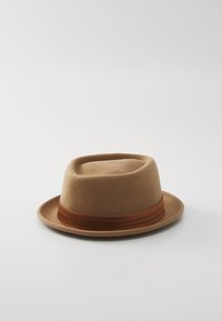 Căciulă fedora din fetru maro, cu o coroană plată și un bor larg, având un accent texturat din panglică maro în jurul bazei coroanei.