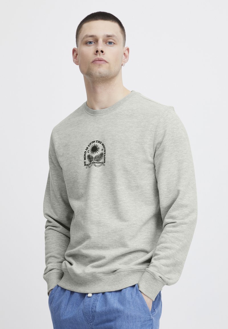 Lys grå sweatshirt laget av en myk bomullsblanding, med lange ermer, ribbede mansjetter og rund hals. Sentral grafisk design i svart.