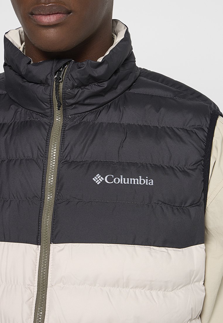 Gilet imbottito con colletto alto, caratterizzato da una parte superiore nera e una parte inferiore beige chiaro. Logo Columbia visibile sul petto.